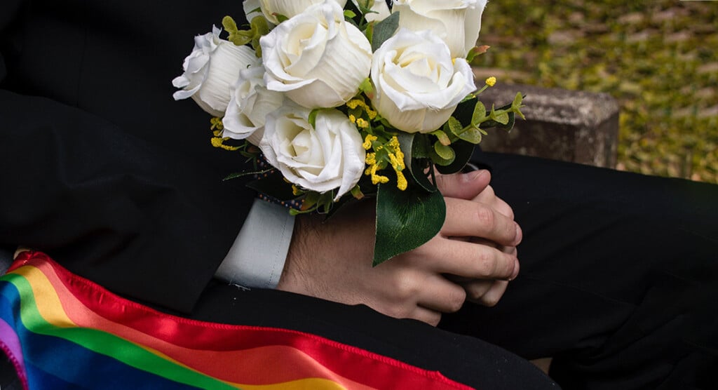 Person holding a bouquet of flowers and a rainbow flag at a wedding.